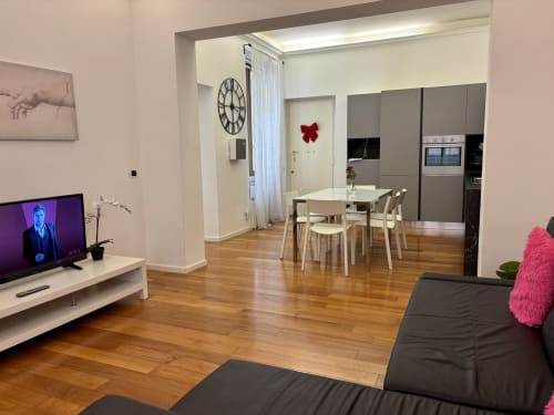 Moderno appartamento open-plan a Domus Caecilia Roma con parquet, zona pranzo, cucina, salotto TV e divano nero