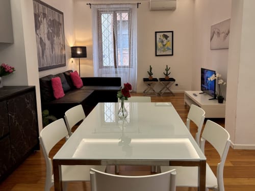 Appartamento moderno a Roma presso Domus Caecilia con zona pranzo, tavolo bianco, divano nero con cuscini rosa e living