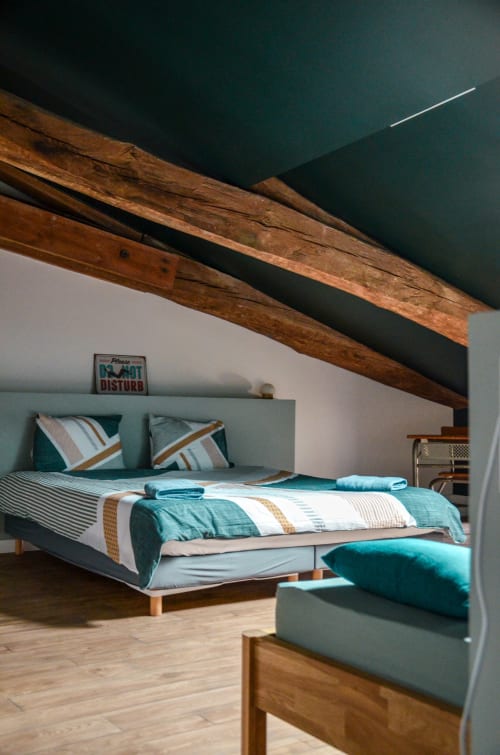 Modern bedroom in La Maison d'Augustin B&B Mont-de-Marsan with teal accents, wooden beams, and striped bedding
