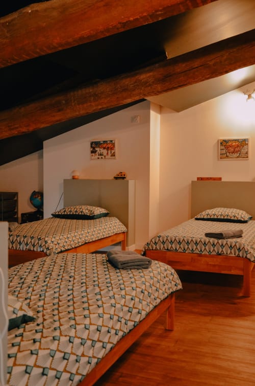 Spacious family apartment bedroom at La Maison d'Augustin in Mont-de-Marsan with three wooden beds, exposed beams, and