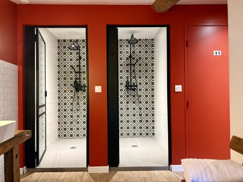 Two modern shower stalls with geometric patterned tiles in a red-walled bathroom at La Maison d'Augustin, Mont-de-Marsan