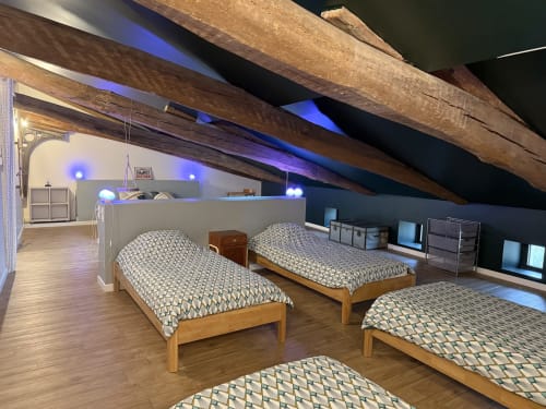 Spacious attic bedroom with four wooden beds, blue accent lighting, exposed beams, and storage at La Maison d'Augustin in