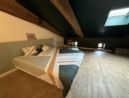 Spacious loft bedroom at La Maison d'Augustin with exposed beams, queen bed, and skylights in Mont-de-Marsan