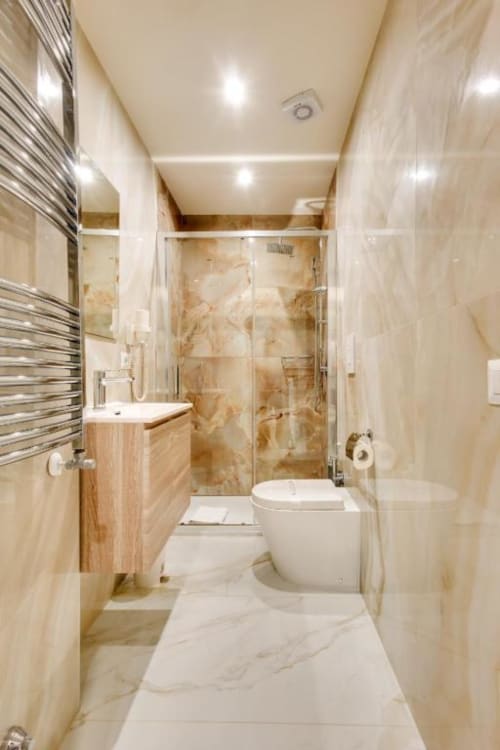 Bagno moderno dell'hotel Domus Praeclara Merulana a Roma con piastrelle in marmo, doccia in vetro, mobile in legno e sanitari bianchi
