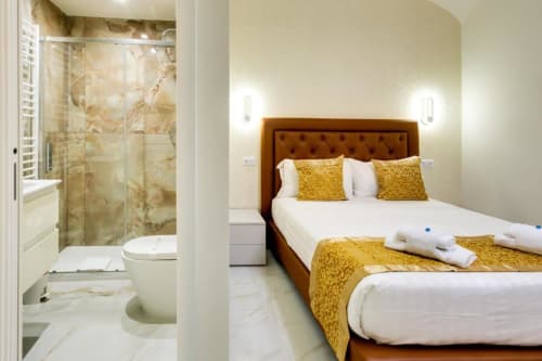 Camera Deluxe King presso Domus Praeclara Merulana a Roma con letto con testiera in pelle marrone e cuscini gialli