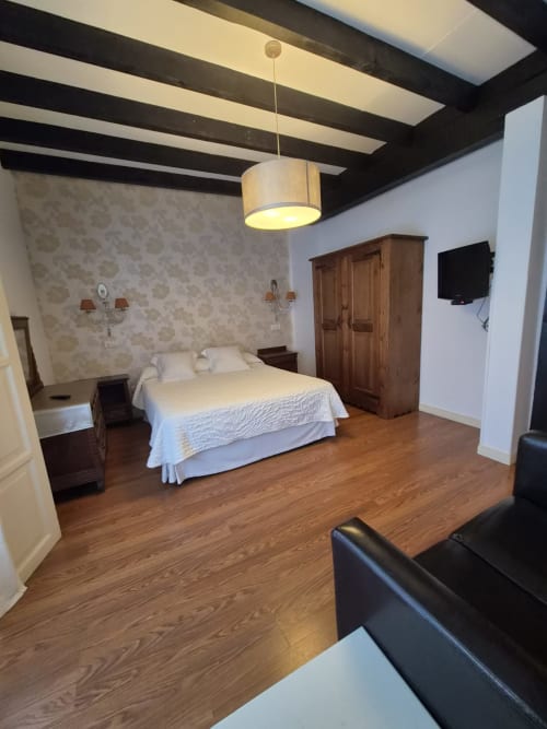 Spacious hotel bedroom at Posada Torre del Milano in Comillas with bed, wooden beams, fireplace, and TV
