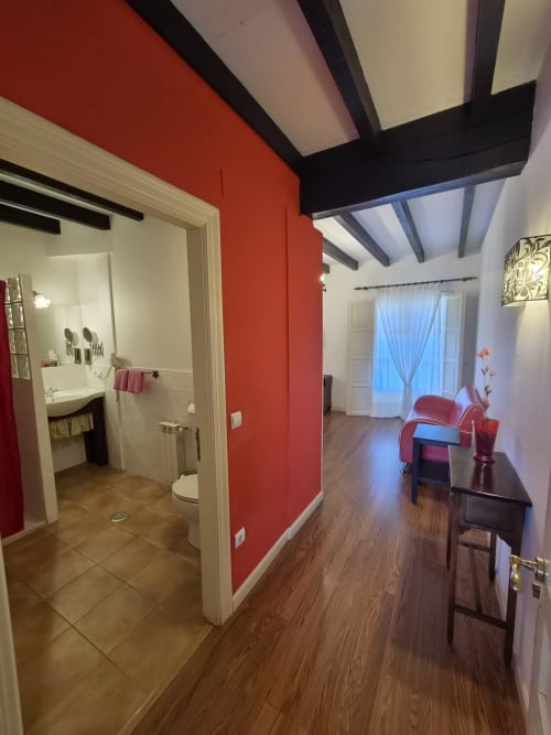 Modern hotel room at Posada Torre del Milano, Comillas with red accent wall, wooden beams, bathroom entry, and seating area