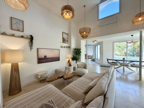 Salon moderne de villa avec mobilier crème, luminaires suspendus tissés et vue sur le jardin à Location Côte Landes