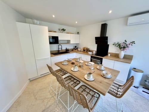 Cuisine moderne et coin repas de la villa LOCATION COTE LANDES avec table en bois, chaises tressées, meubles blancs et noir