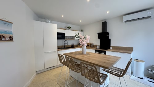 Cuisine moderne et salle à manger de villa dans les Landes avec table en bois, mobilier blanc, hotte noire et fleurs roses