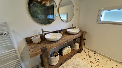 Salle de bains moderne avec deux vasques sur meuble en bois brut, miroirs ronds et sol en terrazzo à LOCATION COTE LANDES
