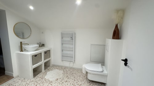 Salle de bain moderne de la villa Cote Landes avec sol en terrazzo, vasque, toilettes, sèche-serviettes chauffant et accessoires décoratifs
