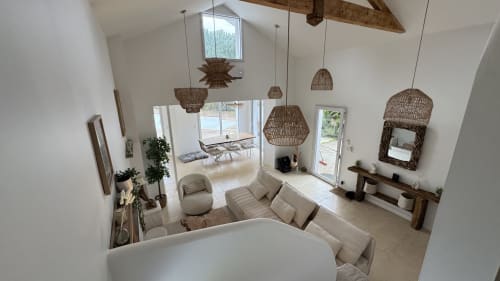 Villa moderne à Côte Landes avec murs blancs, luminaires en rotin, mobilier crème et vue sur la piscine par grandes baies