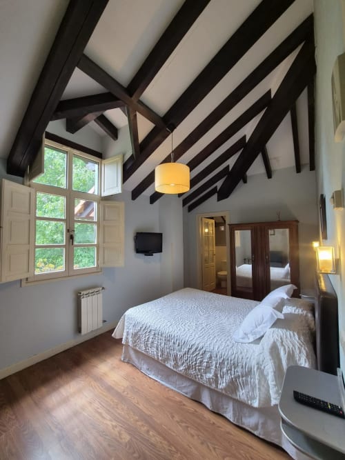Spacious double bedroom at Posada Torre del Milano with exposed beams, white bedding, large windows overlooking gardens, and
