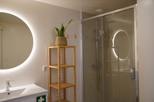 Banheiro moderno no Lumina Apartment em Terra Clara, Esposende com espelhos LED circulares, prateleira de madeira, planta em vaso e