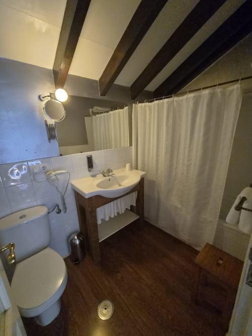 Bathroom with white sink, toilet, shower, dark beams, cream curtains at Posada Torre del Milano, Comillas