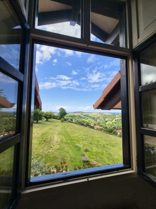 Open window view from Posada Torre del Milano in Comillas showing rolling green hills and mountains under blue sky