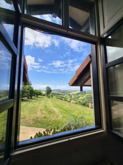 Open window view from Posada Torre del Milano in Comillas showing rolling green hills and blue sky