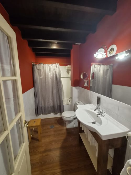 Modern bathroom at Posada Torre del Milano in Comillas with red walls, white sink, toilet, and shower curtain