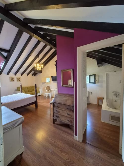 Spacious bedroom at Posada Torre del Milano in Comillas with exposed beams, purple accent wall, and en-suite bathroom