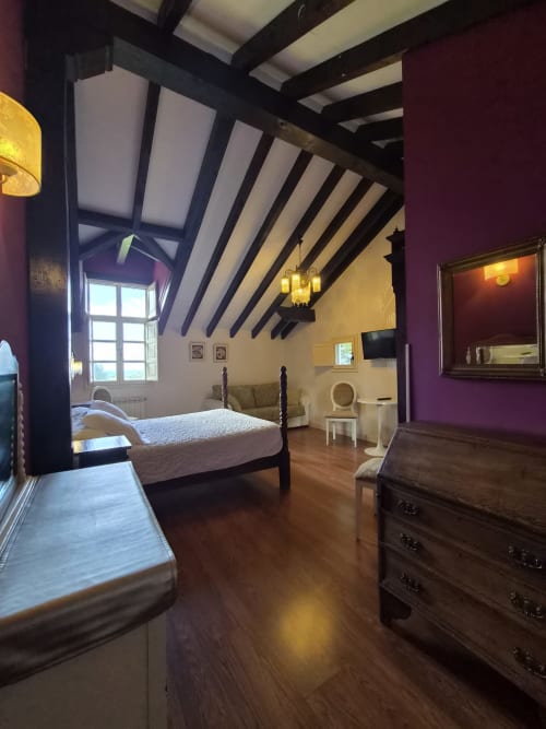 Amplio dormitorio en buhardilla de Posada Torre del Milano en Comillas con vigas vistas, paredes accent en púrpura y suelos de madera
