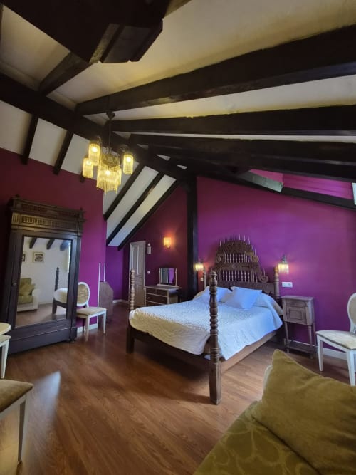Luxurious bedroom at Posada Torre del Milano in Comillas with vibrant purple walls, dark beamed ceiling, and four-poster bed