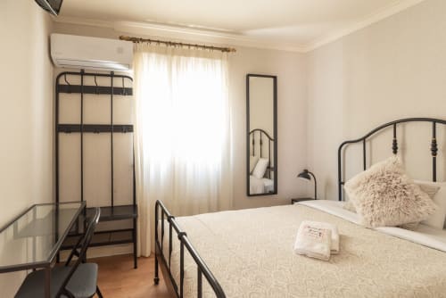 Bright hotel bedroom at Charme da Graça, Lisboa, with metal bed frame, desk, AC unit, and cream curtains