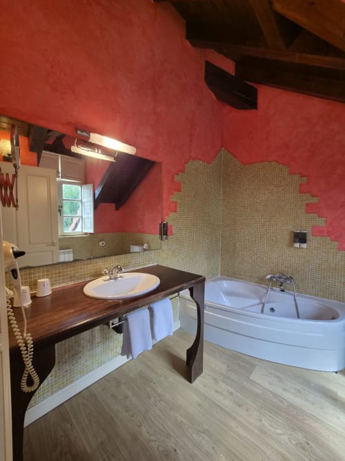 Luxurious bathroom at Posada Torre del Milano with red walls, beige tile, wooden vanity, corner bathtub, and mirror in