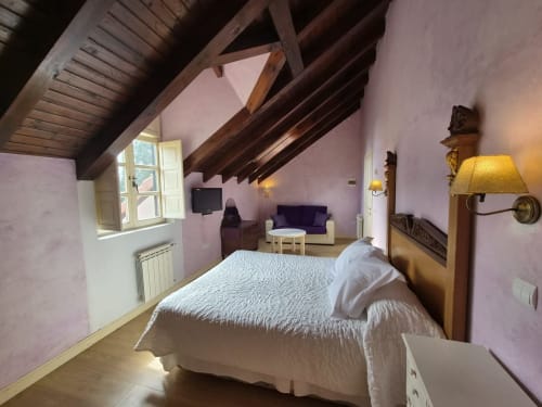 Acogedora habitación doble en Posada Torre del Milano en Comillas con vigas vistas, paredes rosa y vistas al jardín.