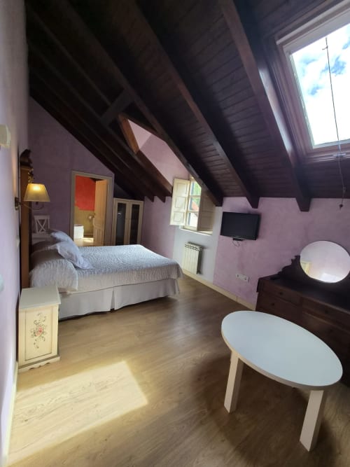 Spacious double bedroom at Posada Torre del Milano in Comillas with lavender walls, exposed wooden beams, and ocean views