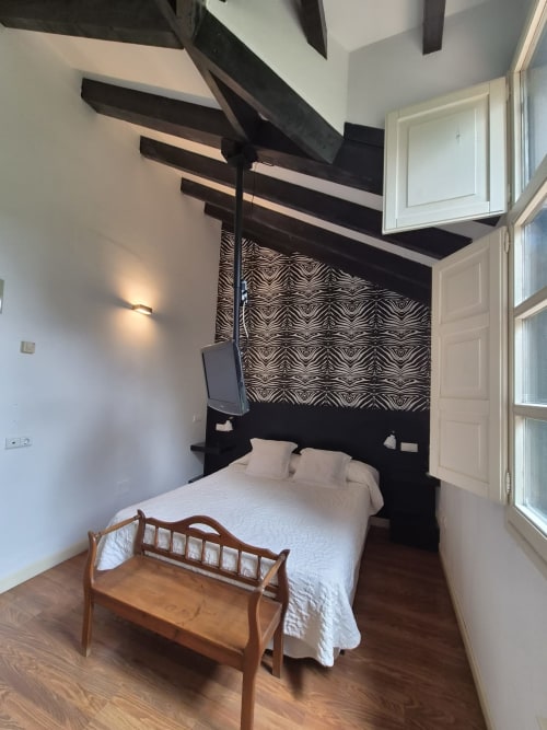 Cozy double room at Posada Torre del Milano in Comillas with exposed beams, zebra-striped headboard, and wooden bench.