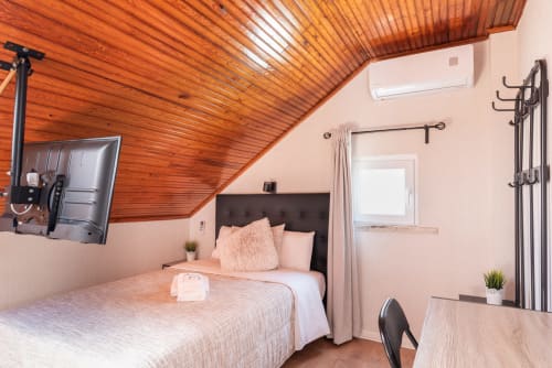 Modern bedroom at Charme da Graça hotel in Costa de Caparica with wooden ceiling, pink walls, and fitness equipment