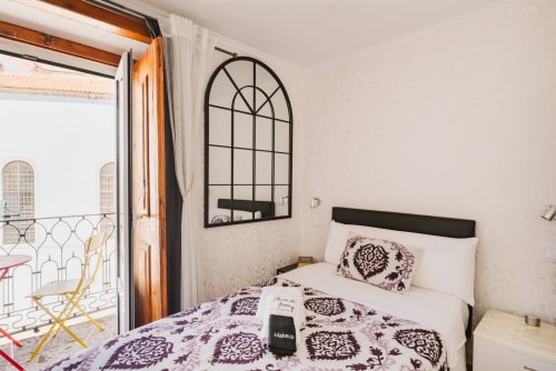 Charme da Graça hotel room in Lisbon with double bed, black headboard, patterned purple bedding, arched mirror, and balcony