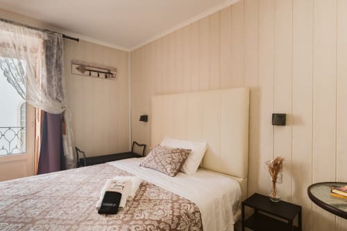 Charme da Graça hotel double bedroom in Lisbon with cream headboard, patterned bedding, window with balcony, and neutral
