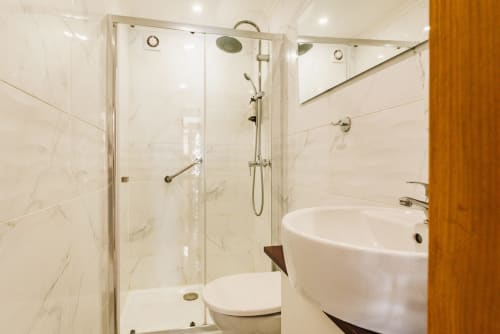 Modern bathroom at Charme da Graça hotel in Lisbon with glass shower enclosure, white marble tiles, and round vessel sink