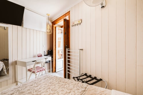 Charme da Graça hotel room in Lisboa featuring a bed, desk with chair, wooden door, and white paneled walls
