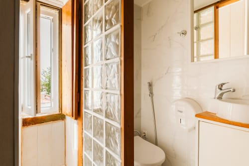 Charme da Graça hotel bathroom in Lisboa with marble walls, glass block shower partition, sink, toilet, and wooden accents