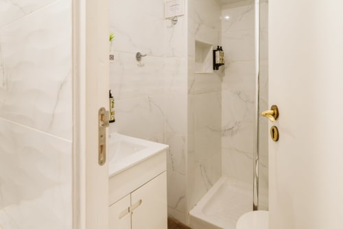 Modern bathroom with marble tiles, white vanity, and glass shower enclosure at Charme da Graça hotel in Lisboa
