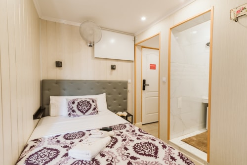 Charme da Graça hotel room with single bed, purple patterned bedding, beige walls, en-suite bathroom, fan, and modern