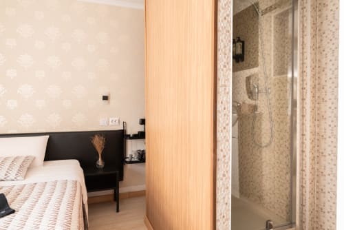 Charme da Graça hotel room in Lisboa with en-suite shower, wooden door dividing bedroom from bathroom with beige tile walls