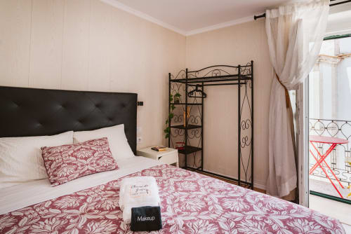 Charme da Graça hotel room in Lisboa with burgundy patterned bedding, black headboard, wrought iron wardrobe, and balcony