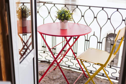 Red circular table with potted plant on Charme da Graça balcony in Lisbon, yellow chair visible