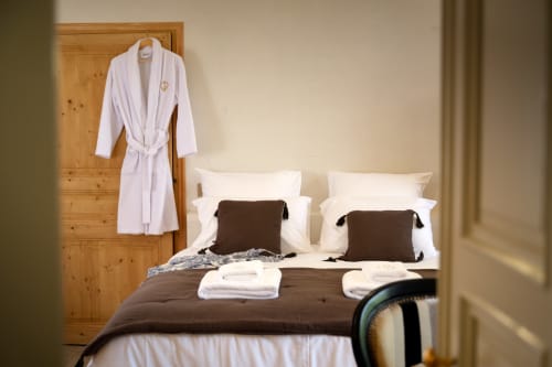 Chambre à la Ferme Saint-Georges avec peignoirs blancs, literie marron et oreillers blancs en Provence