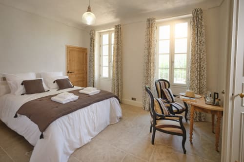 Chambre élégante à la Ferme Saint-Georges en Provence, vue sur le jardin, literie marron et blanc, rideaux à motifs, boiseries