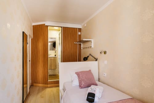 Charme da Graça hotel room 11 in Lisboa: single bed with pink cushion, wooden wardrobe, ensuite bathroom, desk, and city view