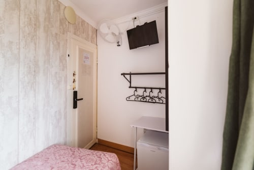 Small single room at Charme da Graça hotel in Lisbon with pink bedding, TV, wall-mounted shelf, fan, and wooden flooring