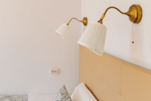 Two elegant brass wall sconces with pleated white shades above a bed at Charme da Graça hotel in Lisbon