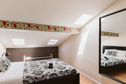 Modern attic bedroom at Charme da Graça, Lisboa with patterned bedding, skylight windows, decorative border, and large mirror