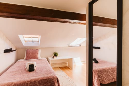 Charme da Graça attic bedroom in Lisbon with pink bedding, skylights, wooden beams, and mirror