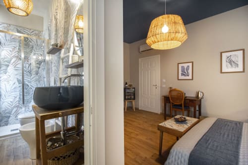 Camera da letto Epimoni B&B a Catania con scrivania, letto, lampada a sospensione intrecciata e bagno ensuite con piastrelle doccia tropicali
